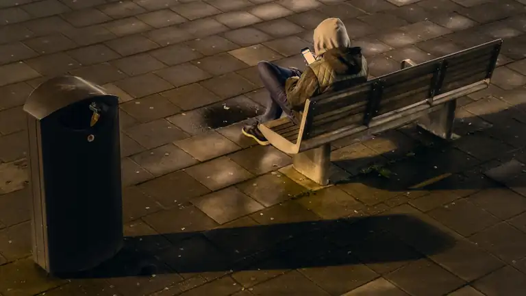 A person in a hoodie sitting alone on a bench at night